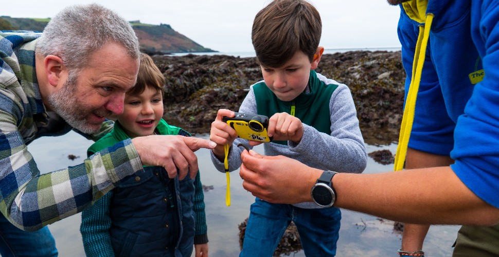 Group of children and adults looking at a find from a rock pool, and taking a photo